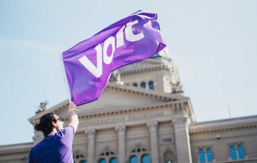 Person, die eine violette Volt Flagge vor dem Bundeshaus schwingt